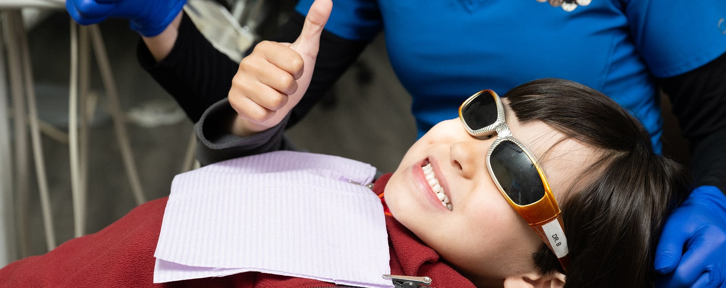 A boy in a glasses is smiling in a dental chair