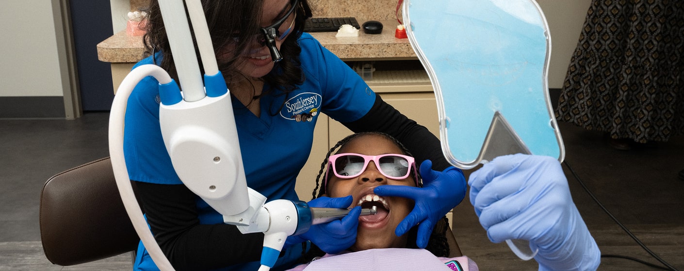 Dentist is smiling together with a child in a dental chair while performing dental procedure