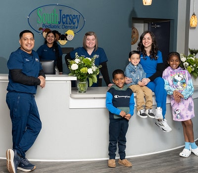 Happy South Jersey pediatric dental team smiling with young kids at front desk