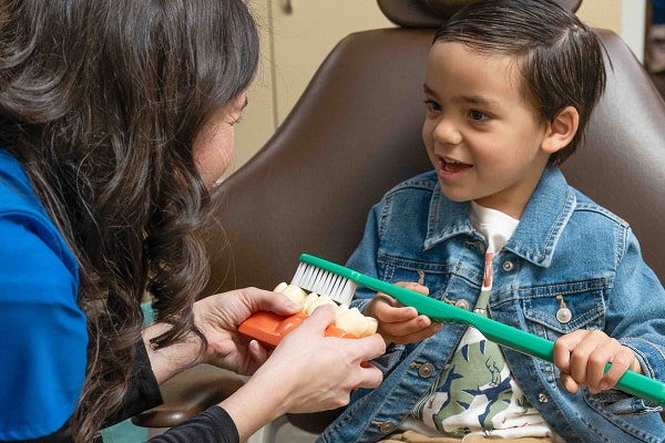A boy is smiling with Dr. Brendaliz while learning how to brush teeth