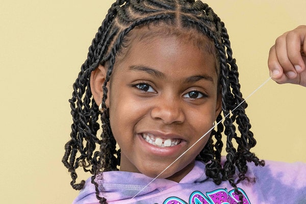 A girl is smiling and holding dental floss