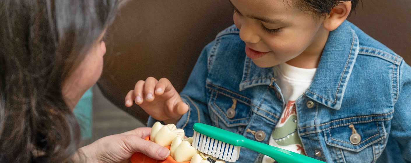 A happy kid is smiling and looking at a model of a tooth-brush