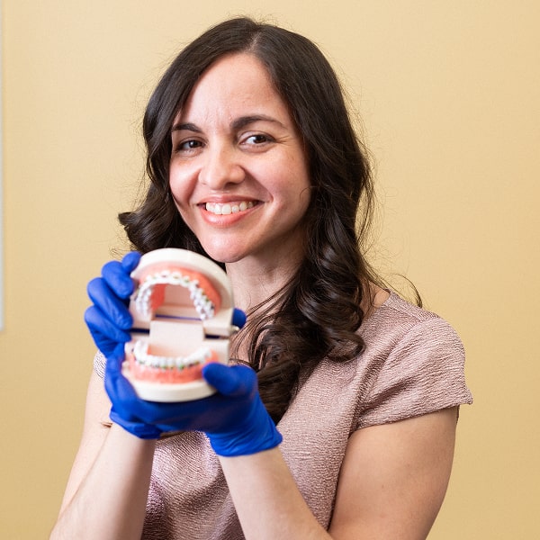 A woman is happily smiling while showcasing model of a jaw with braces