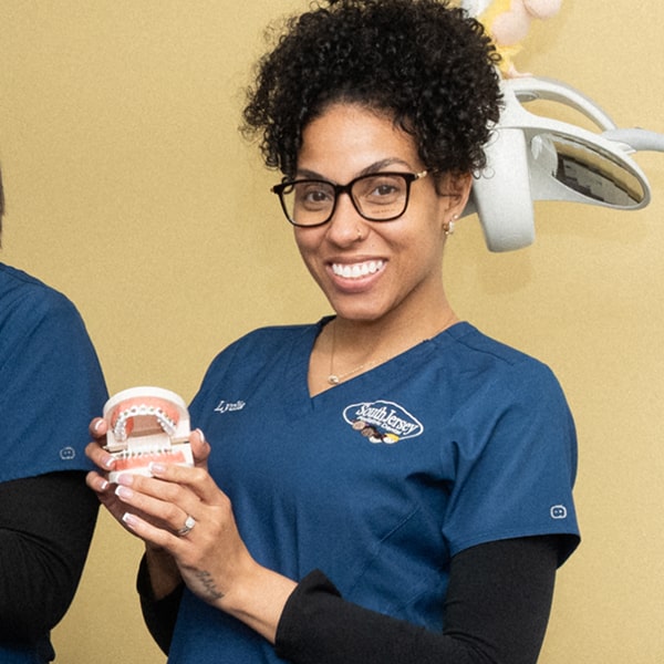 Dentist from South Jersey is smiling while holding dental model of a jaw with braces