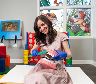 Dentist with a huge toothbrush and a model of a jaw is smiling at South Jersey Pediatrics